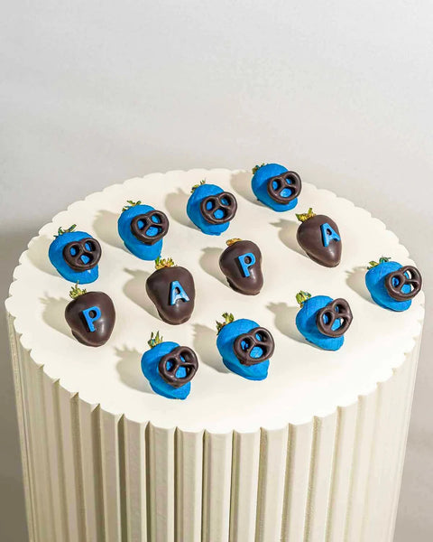 Decorative cake with chocolate-covered strawberries shaped like faces and letters on a white background