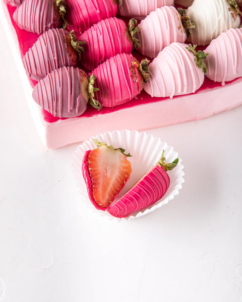 Pink and white chocolate-dipped strawberries on a pink tray with a single strawberry in a white paper cup.
