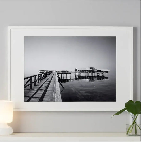 Black and white framed wall art of a wooden pier over calm water, minimalist home decor